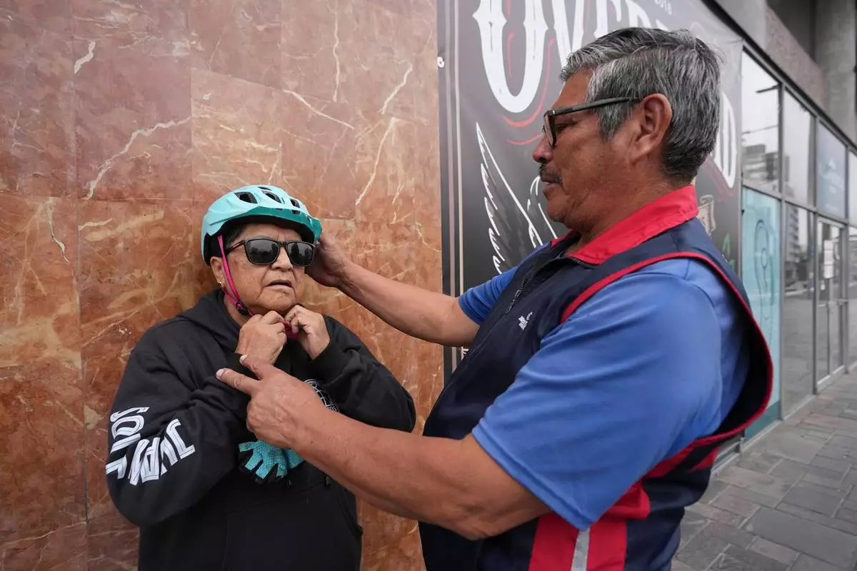 A volunteer helps a visually impaired participant put on a helmet before a bicycle ride with the "Ciegocleta" initiative in Quito, Ecuador, Sunday, Aug. 30, 2026. (AP Photo/Dolores Ochoa)