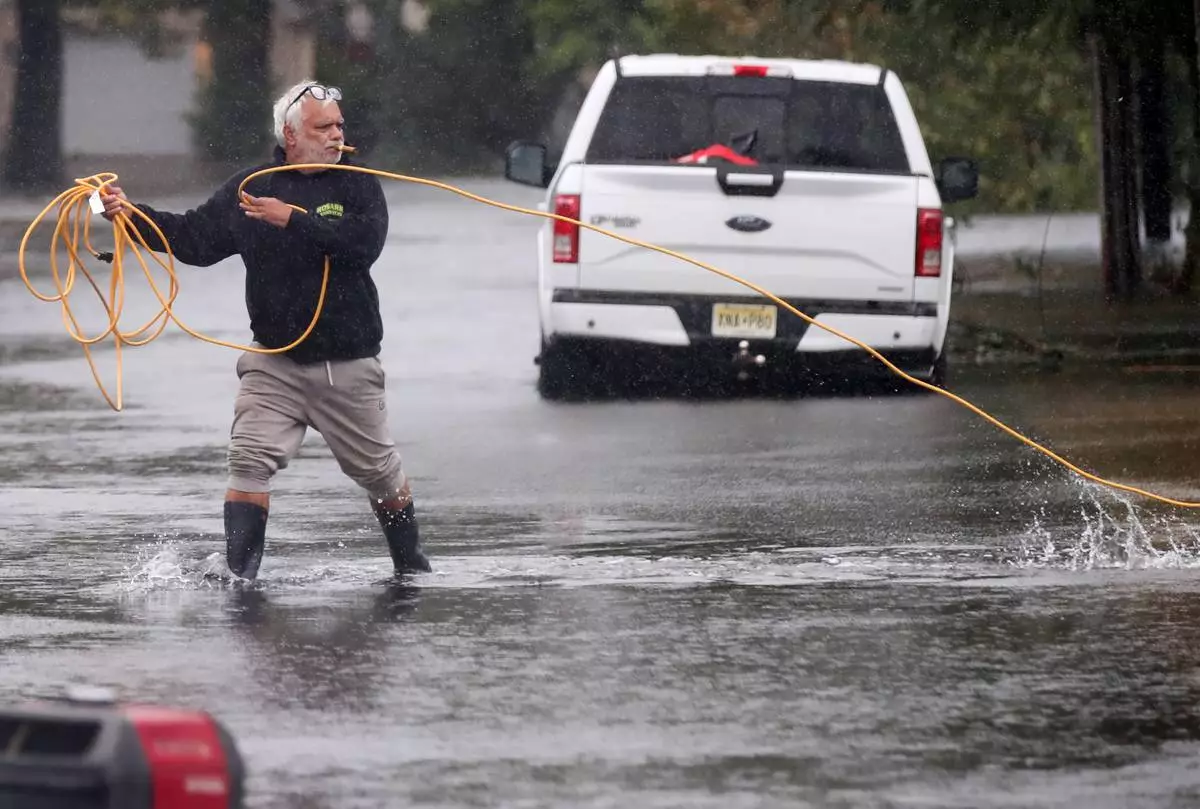 Jose Rosario pulls an extension cord out of his flooded garage to connect to a generator on Catherine St. Saturday, Sept. 26, 2026, in Long Branch, N.J. (AP Photo/Noah K. Murray)