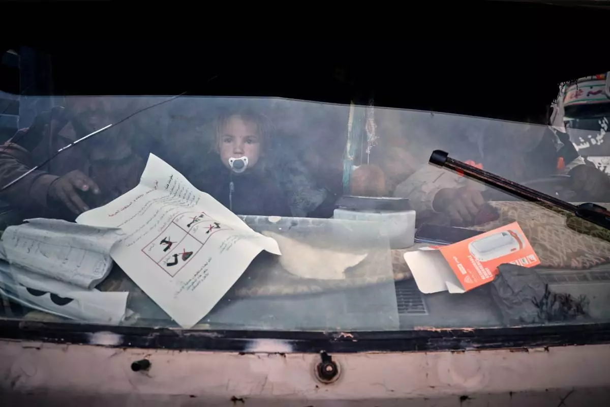 A young child looks through a truck's windshield as displaced families prepare to leave al-Talayi camp in Hassakeh, Syria, Tuesday, Oct. 13, 2026. Around 450 families are returning to the Ras al-Ayn countryside, seven years after a Turkish military offensive forced them to flee. (AP Photo/Baderkhan Ahmad)