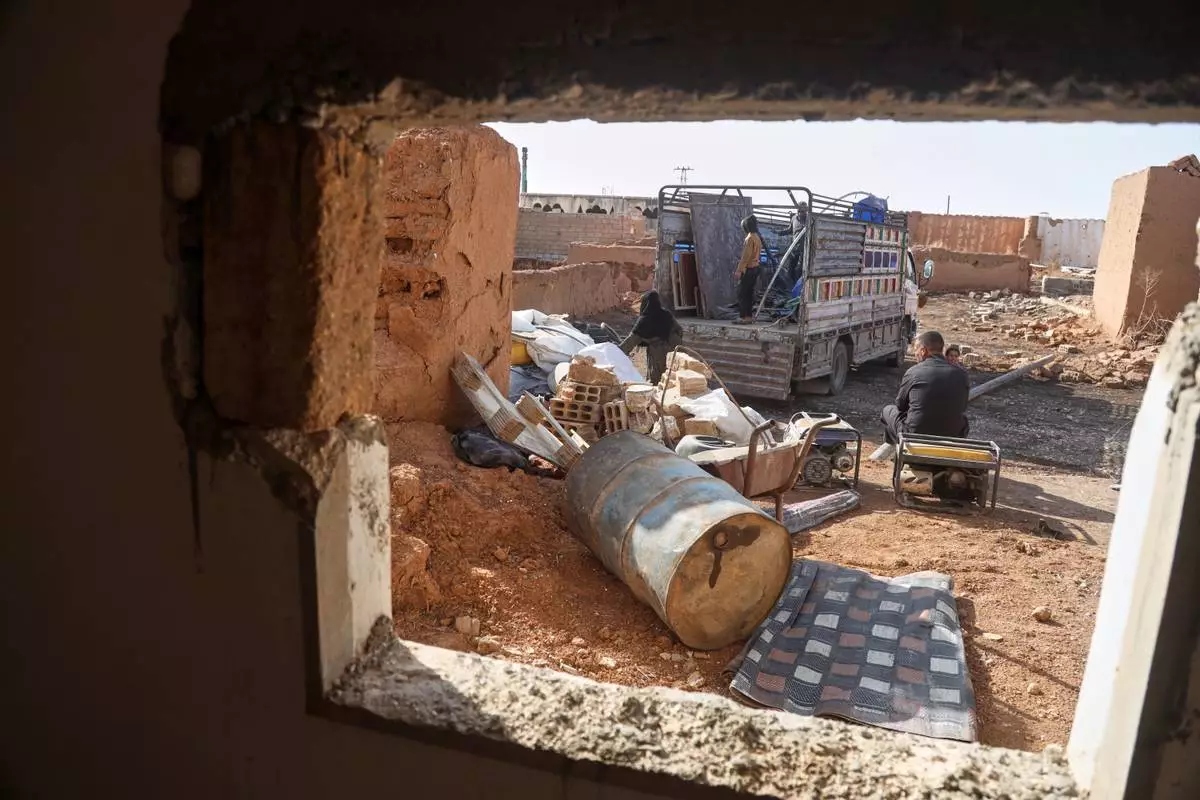Returning residents unload belongings from a truck amid damaged buildings in Al-Arisha, in Syria's Ras al-Ayn countryside, Tuesday, Oct. 13, 2026, seven years after a Turkish military offensive backed by allied Syrian factions forced them to flee. (AP Photo/Baderkhan Ahmad)