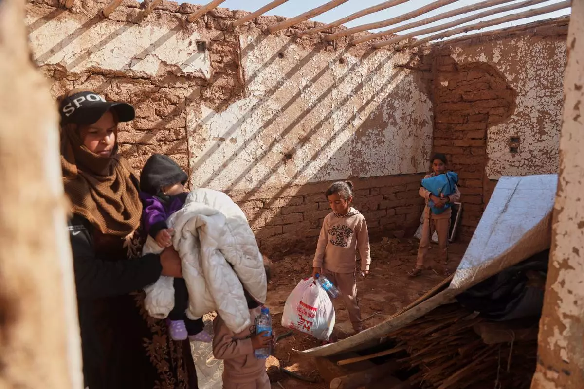 A woman holds a young child as other children carry belongings inside their damaged home after returning to Al-Arisha, in Syria's Ras al-Ayn countryside, Tuesday, Oct. 13, 2026, seven years after a Turkish military offensive alongside allied Syrian factions forced them to flee. (AP Photo/Baderkhan Ahmad)