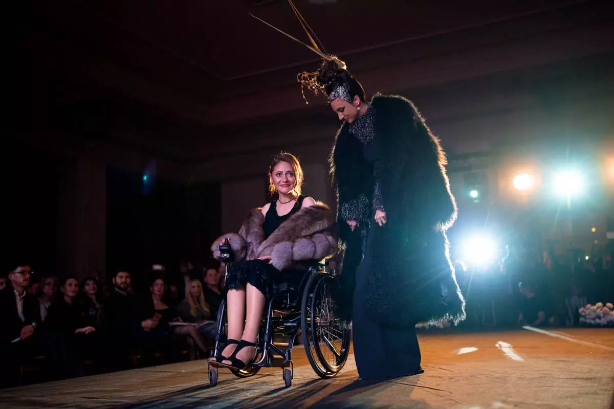 Ana Mihaela Stancu, a wheelchair user, is accompanied by a model during the Atypic Beauty Gala fashion show, an event promoting inclusion and equal opportunities for people with disabilities, in Bucharest, Romania, Thursday, Oct. 22, 2026. (AP Photo/Andreea Alexandru)