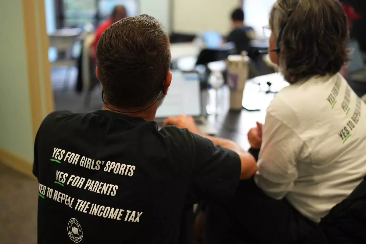 Let's Go Washington staff member Josh Johnson, left, helps a volunteer while phone banking in support of Washington State Initiative 638, which would prohibit transgender girls from competing in girls' sports, Monday, Oct. 19, 2026, in Bellevue, Wash. (AP Photo/Lindsey Wasson)