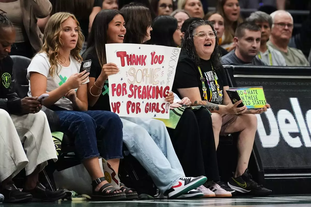 FILE- Ahnaleigh Wilson, 17, a track athlete who says she has competed against and placed behind transgender athletes at meets, holds a sign for Indiana Fever guard Sophie Cunningham in reference to her comments on transgender athletes during the first half of a WNBA basketball game between the Fever and Seattle Storm, Tuesday, July 28, 2026, in Seattle. (AP Photo/Lindsey Wasson, File)