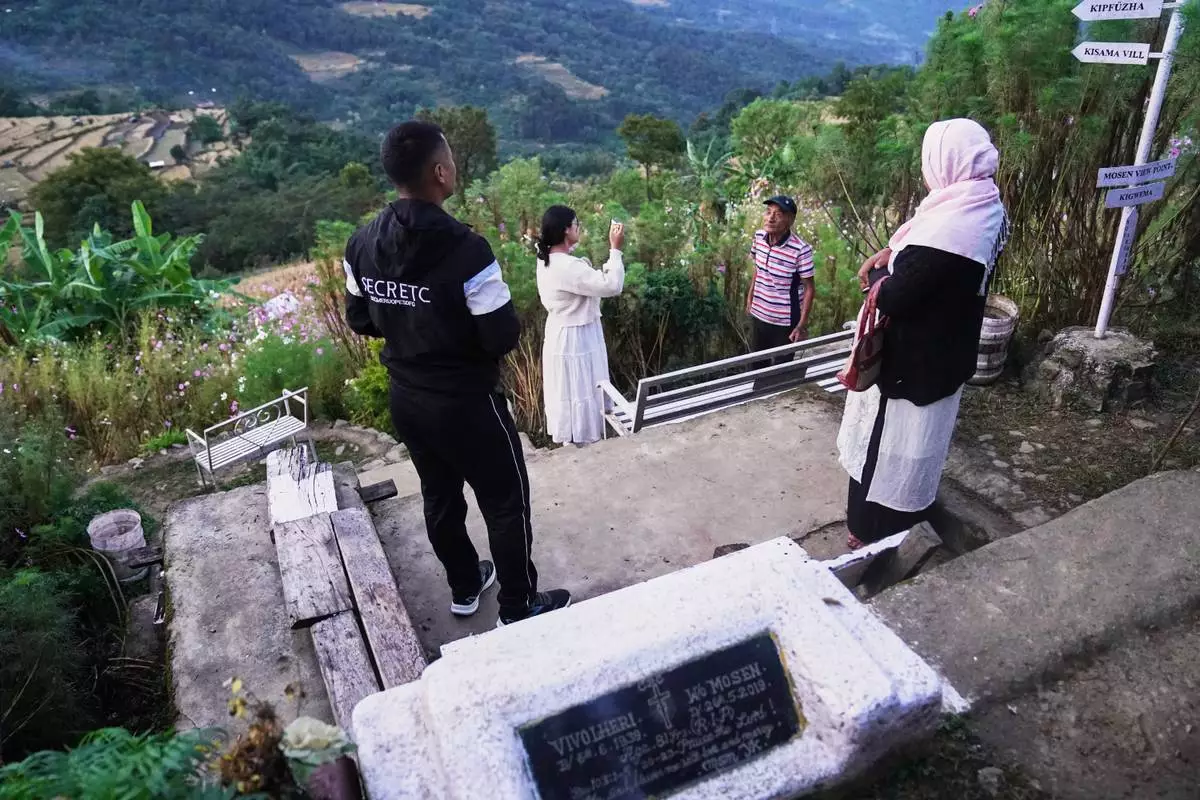 Tourists speak with Mosenyii Yakhro, 90, in the garden he started by his wife's grave, seen in foreground, in Kigwema village, in the northeastern Indian state of Nagaland, Tuesday, Oct. 27, 2026. (AP Photo/Yirmiyan Arthur)