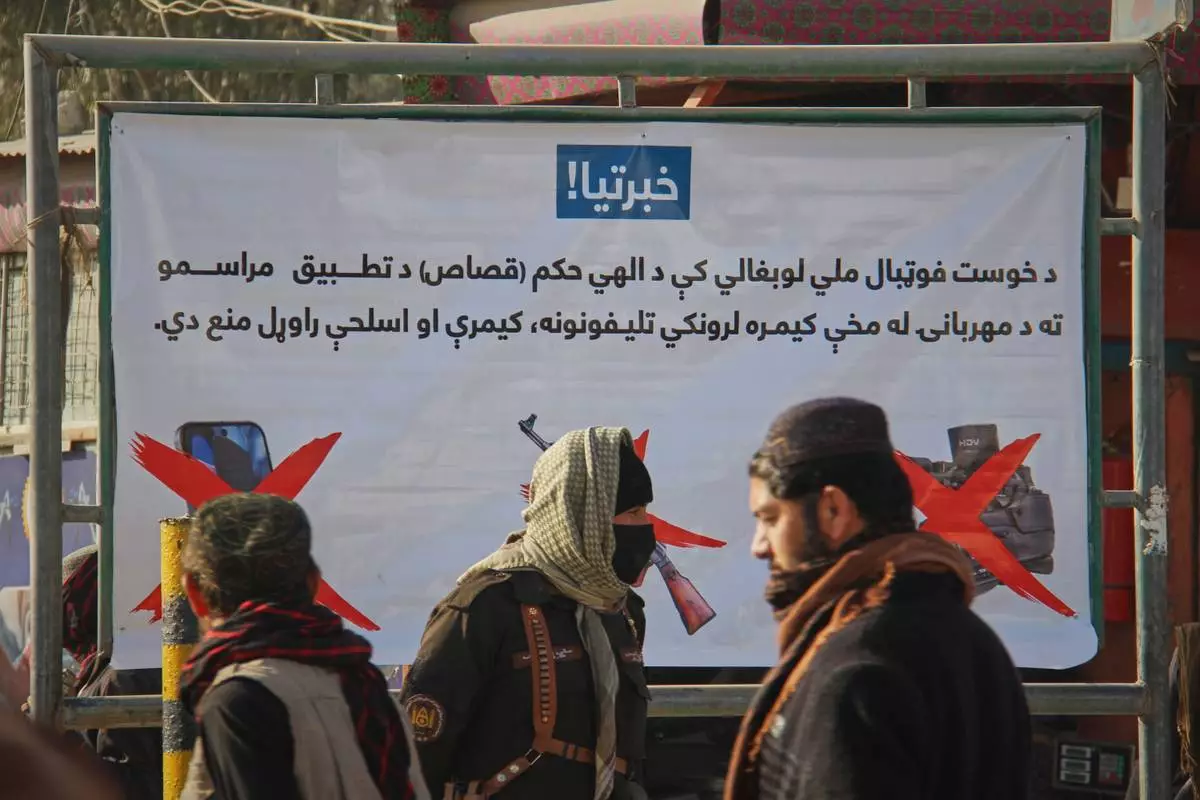 FILE - A Taliban policeman, center, and two other men walk past a poster stating that cameras, phones, and weapons are banned inside a stadium where a public execution was taking place in the city of Khost, eastern Afghanistan, Dec. 2, 2025. (AP Photo/Saifullah Zahir, File)