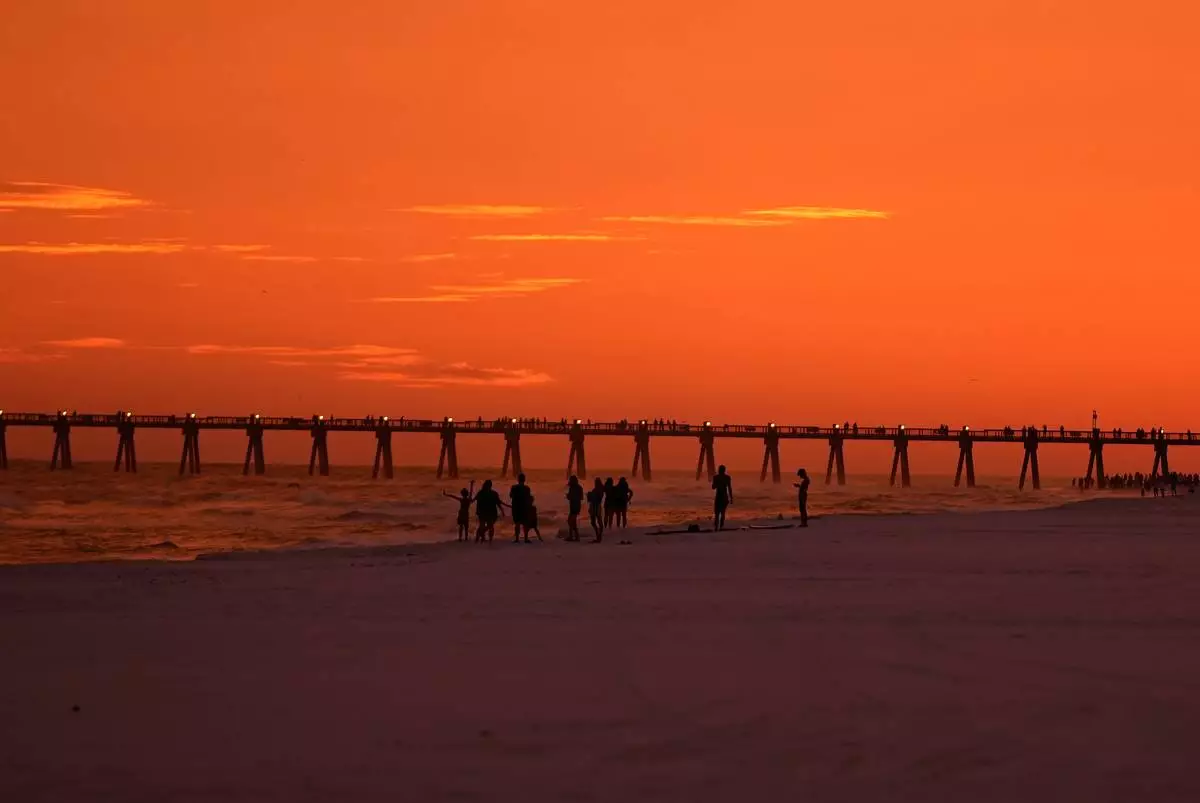 People walk on the beach at sunset as Hurricane Isaias approaches Pensacola Beach, Fla., Thursday, Oct. 8, 2026. (AP Photo/Gerald Herbert)