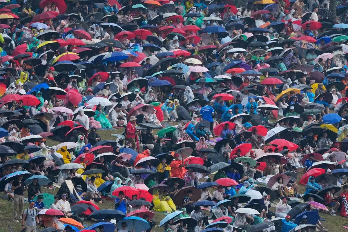Spectators with umbrella and rain covers gather on a hillside to watch the Bahrain Grand Prix in Sepang, Malaysia, Sunday, Oct. 4, 2026. (AP Photo/Vincent Thian)