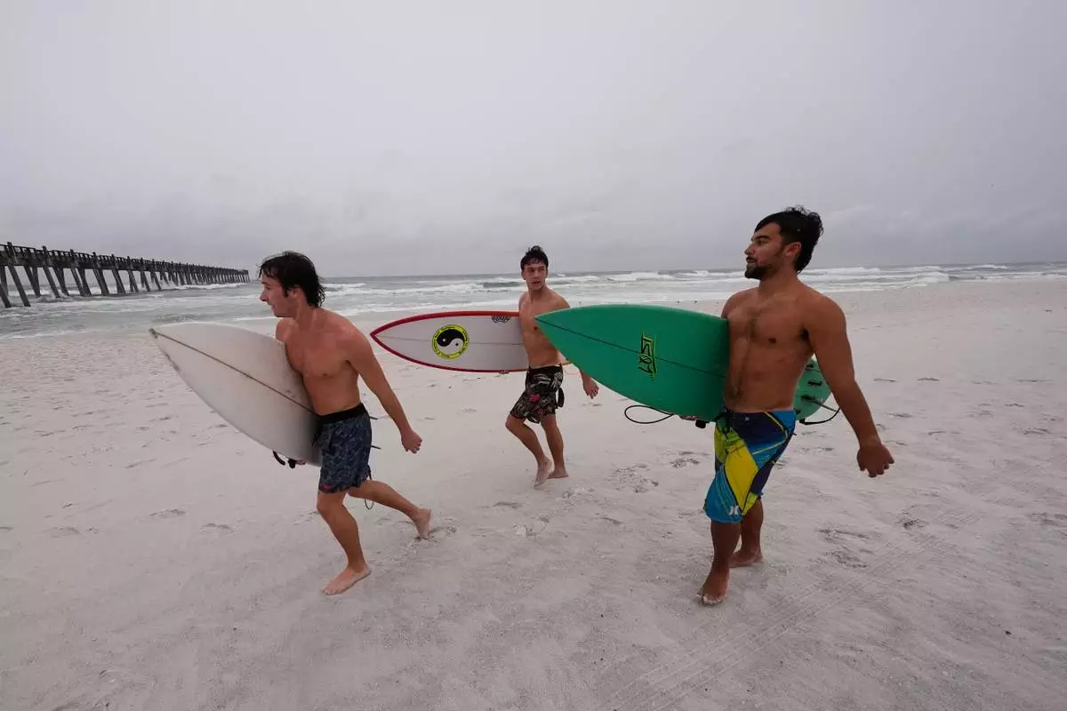 Surfers walk along the beach as Hurricane Isaias approaches Pensacola Beach, Fla., Friday, Oct. 9, 2026. (AP Photo/Gerald Herbert)