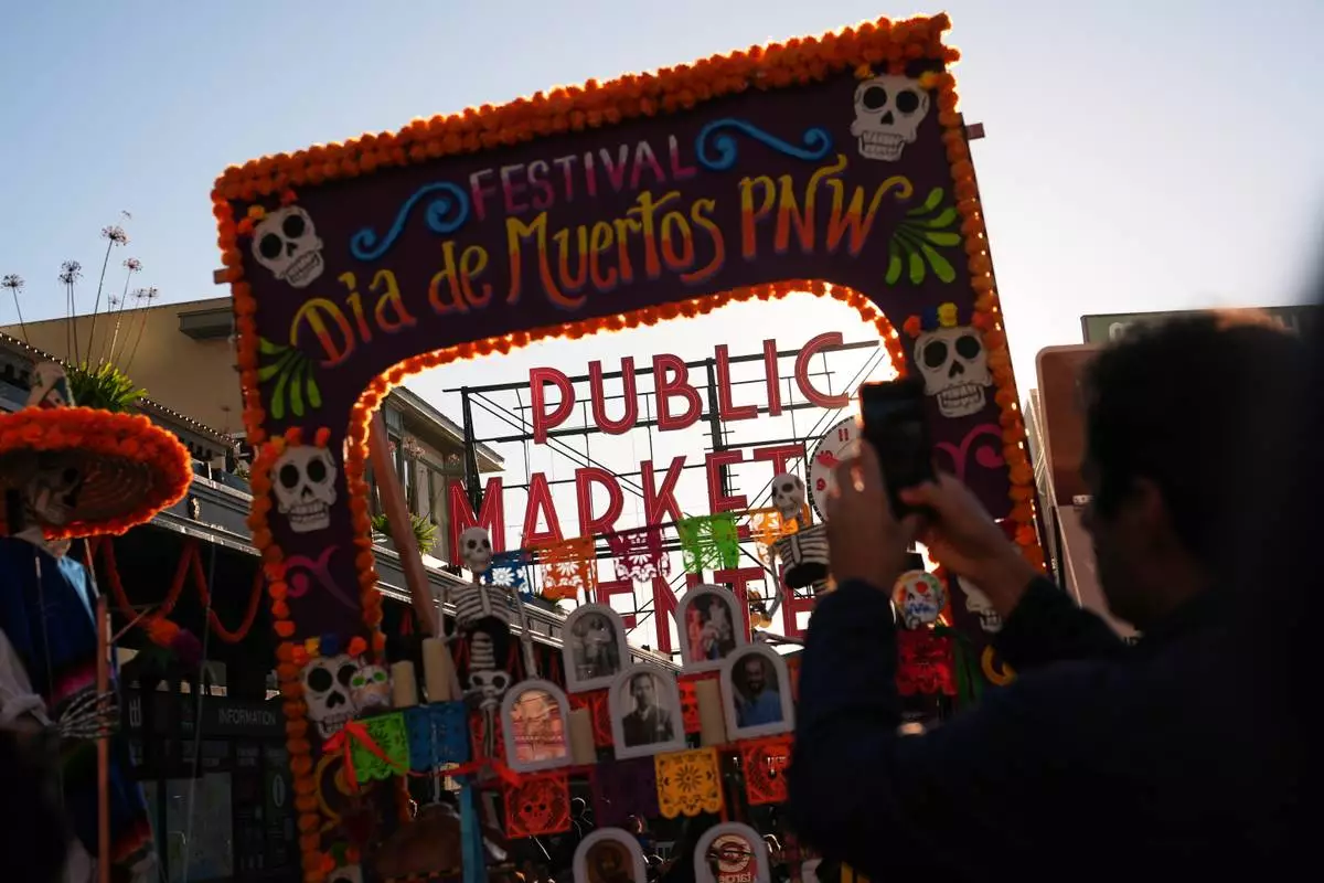 People take photos of the main Pike Place Market sign behind an ofrenda during a Día de Muertos celebration, Friday, Oct. 23, 2026, in Seattle. (AP Photo/Lindsey Wasson)