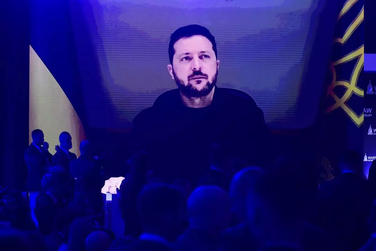 People watch Ukrainian President Volodymyr Zelenskyy on a large screen as he speaks to the Warsaw Security Forum in Warsaw, Poland, Monday, Oct. 12, 2026. (AP Photo/Attila Husejnow)
