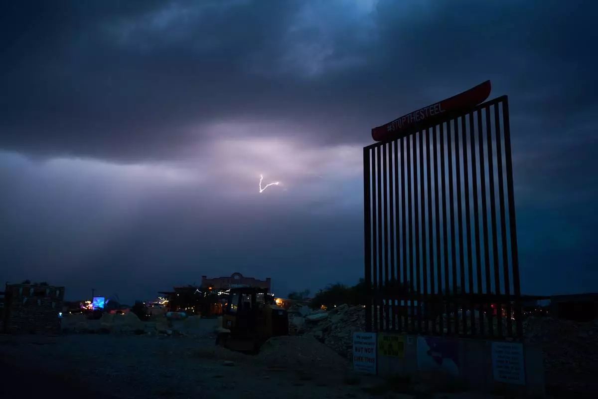 Lightning illuminates the sky behind a mockup of the border wall in protest of proposed barriers along the border, Thursday, Sept. 24, 2026, in Terlingua, Texas. (AP Photo/John Locher)
