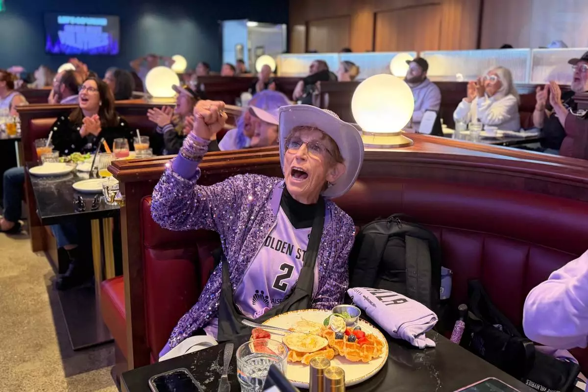 Golden State Valkyries fan Cynthia Cheak cheers over breakfast at Splash restaurant at Chase Center's Thrive City plaza, Thursday morning, Oct. 29, 2026, in San Francisco, as fans gather to watch a broadcast of Game 6 of the WNBA basketball finals against the Atlanta Dream. (AP Photo/Janie McCauley) Photo taken with a smartphone.
