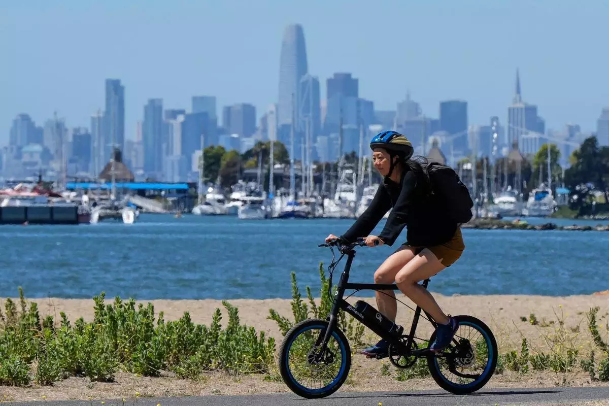 (美聯社圖片/戈多弗雷多A.華斯基斯) 2025年8月19日，加州阿拉米達，一名女子在小徑上騎單車，背景可見三藩市（San Francisco）天際線。 AP圖片