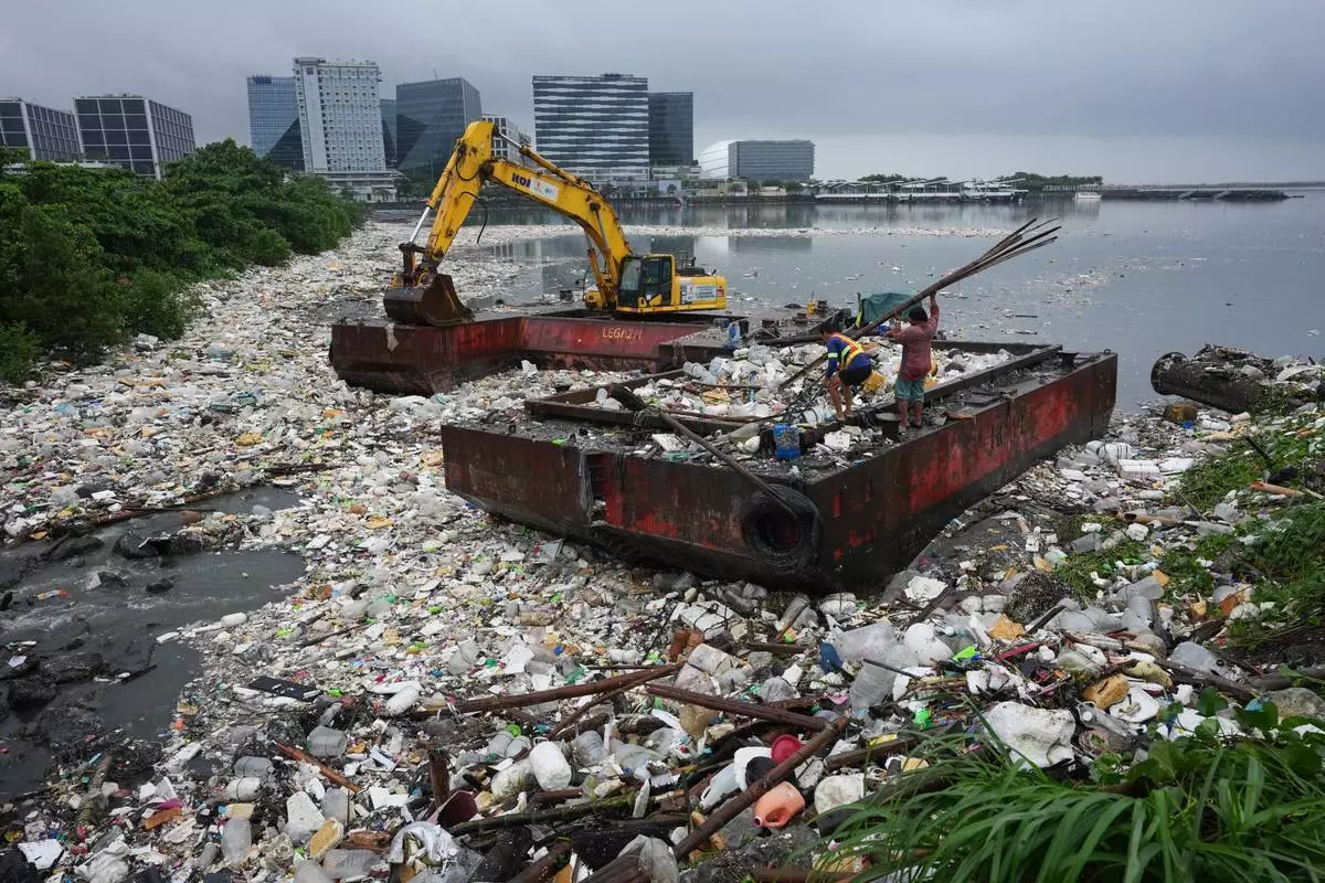 2026年8月12日周三，菲律賓馬尼拉大都會帕賽市，工人搬運竹子，旁邊是因強烈季候雨沖上岸的垃圾海。(美聯社圖片/Aaron Favila) AP圖片