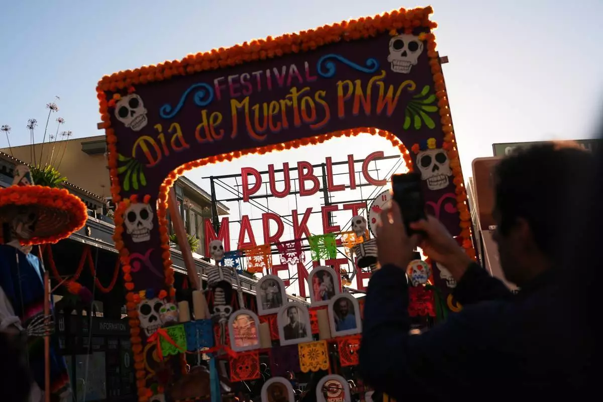 周五（2026年10月23日），人們在西雅圖亡靈節慶祝活動期間，於一個祭壇（ofrenda）後方拍攝派克市場主標誌。(美聯社圖片/Lindsey Wasson) AP圖片