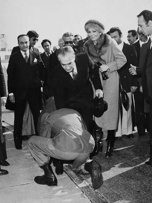 FILE - In this Jan. 16, 1979 file photo, a soldier bends to kiss the feet of Iran's Shah Mohammad Reza Pahlavi on the tarmac of Mehrabad Airport in Tehran, Iran. Behind the shah is his wife, Empress Farah. Wednesday, Jan. 16, 2019 marks the 40th anniversary of the shah abandoning his Peacock Throne and leaving his nation for the last time in his life, setting the stage for the country's 1979 Islamic Revolution only a month later. (AP Photo, File)