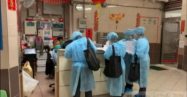 穿著全副防護裝備的衞生防護中心人員，逐家逐戶到康美樓拍門，了解居民身體情況。（林家萍攝）