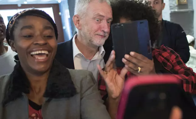 Britain's opposition Labour Party leader Jeremy Corbyn, centre, poses for selfies as he meets people from the Caribbean and the West Indies, members of the Stockwell Good Neighbours community group, in Kennington, south London, Monday April 30, 2018. (Stefan Rousseau/PA via AP)
