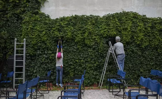 In this Friday May 29, 2020 photo Christina Tsouta, left, cuts leaves as projector operator Pavlos Lepeniotis connects the speakers at the Zephyros open-air cinema that specializes in films from past decades in Athens' central Petralona district. (AP PhotoPetros Giannakouris)
