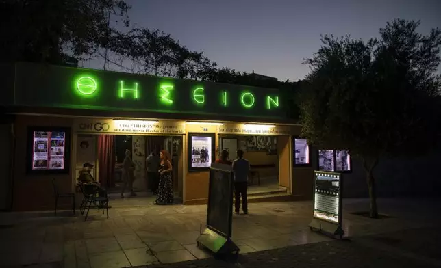 In this Thursday June 4 , 2020 photo passers by looks at movie notices outside the Thision outdoor summer cinema where moviegoers watch films under the ancient Acropolis. Cine Thision is one of the oldest open-air movie theaters in Athens, built in 1935. (AP PhotoPetros Giannakouris)