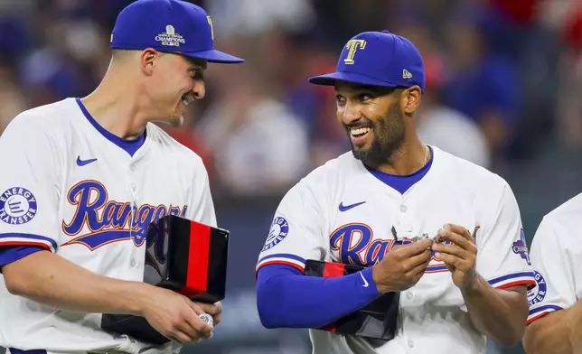 Texas Rangers' Corey Seager, left, and Marcus Semien, right, review their World Series rings before a baseball game against the Chicago Cubs, Saturday, March 30, 2024, in Arlington, Texas. (AP Photo/Gareth Patterson)