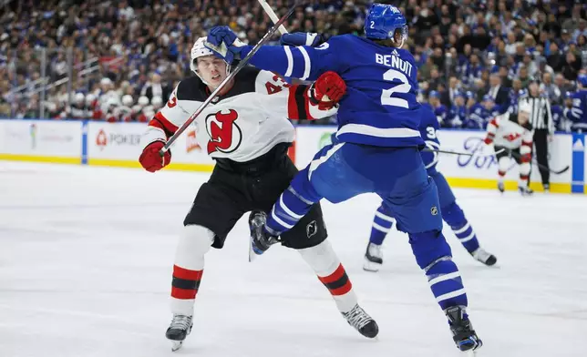 New Jersey Devils defenseman Luke Hughes (43) and Toronto Maple Leafs defenseman Simon Benoit (2) collide during the third period of an NHL hockey game in Toronto on Tuesday, March 26, 2024. (Cole Burston/The Canadian Press via AP)