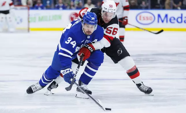 Toronto Maple Leafs center Auston Matthews (34) and New Jersey Devils left wing Erik Haula (56) battle for the puck during the first period of an NHL hockey game in Toronto on Tuesday, March 26, 2024. (Cole Burston/The Canadian Press via AP)