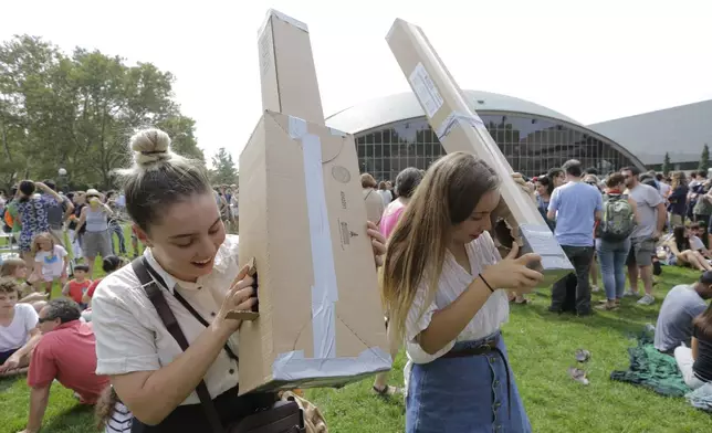 FILE - Reveka Pasternak, of Boston, left, and her sister Tristen, of Philadelphia, right, use pinhole projectors to view a partial solar eclipse, Monday, Aug. 21, 2017, on the campus of Massachusetts Institute of Technology, in Cambridge, Mass. The sisters made the pinhole projectors from cardboard that allow people to safely view the eclipse. (AP Photo/Steven Senne, File)