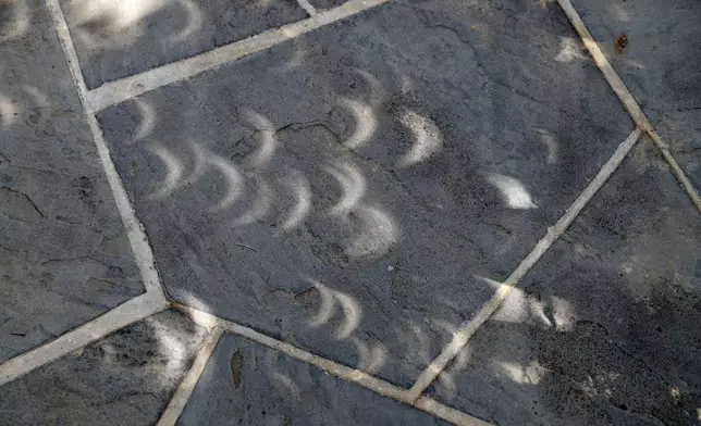 FILE - Projected images of the eclipse are seen through the leaves on the trees on the sidewalk at the White House in Washington, Monday, Aug. 21, 2017. (AP Photo/Alex Brandon, File)