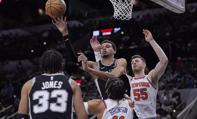 San Antonio Spurs center Victor Wembanyama, center, passes the ball over New York Knicks guard Jalen Brunson (11) during the second half of an NBA basketball game in San Antonio, Friday, March 29, 2024. (AP Photo/Eric Gay)