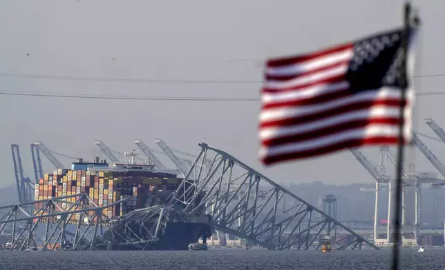 An American flag flies on a moored boat as the container ship Dali rests against wreckage of the Francis Scott Key Bridge, Tuesday, March 26, 2024, as seen from Pasadena, Md. (AP Photo/Mark Schiefelbein)