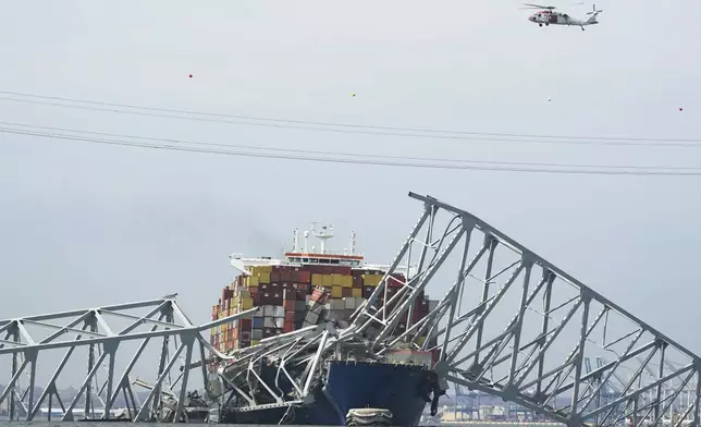 A Coast Guard helicopter passes a cargo ship that is stuck under the part of the structure of the Francis Scott Key Bridge after the ship his the bridge Tuesday March 26, 2024, in Baltimore, Md. (AP Photo/Steve Helber)