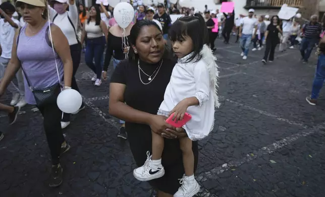 A woman carries her daughter during a demonstration protesting the kidnapping and killing of an 8-year-old girl, in the main square of Taxco, Mexico, Thursday, March 28, 2024. Hours earlier a mob beat a woman to death because she was suspected of kidnapping and killing the young girl. (AP Photo/Fernando Llano)