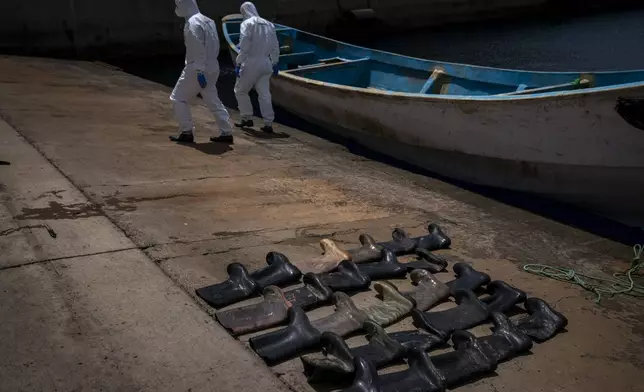 FILE - Rain boots are placed on the ground by police officers as they inspect a boat where 15 Malians were found dead adrift in the Atlantic on Thursday, Aug. 20, 2020, in Gran Canaria island, Spain. The UN migration agency marks a decade since the launch of the Missing Migrants Project, documenting more than 63,000 deaths around the world. More than two-thirds of victims remain unidentified highlighting the size of the crisis and the suffering of families who rarely receive definitive answers. (AP Photo/Emilio Morenatti, File)