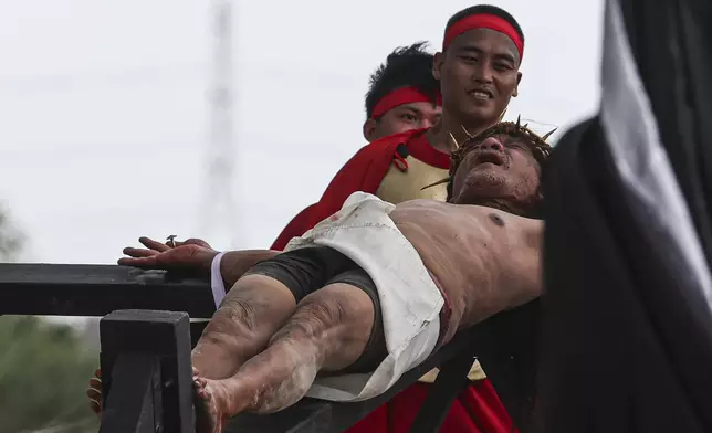 Ruben Enaje grimaces from being nailed to the cross during the reenactment of Jesus Christ's sufferings as part of Good Friday rituals in the San Pedro Cutud, north of Manila, Philippines, Friday, March 29, 2024. The Filipino villager was nailed to a wooden cross for the 35th time to reenact Jesus Christ’s suffering in a brutal Good Friday tradition he said he would devote to pray for peace in Ukraine, Gaza and the disputed South China Sea. (AP Photo/Gerard V. Carreon)