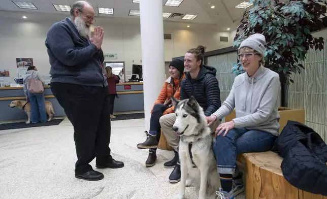 In this image provided by WSU College of Veterinary Medicine, Scott Campbell, left, the veterinary chaplain at Washington State University's College of Veterinary Medicine, visits with Olivia and Phinehas Lampman, center, owners of Goose, a Husky mix dog, as Phinehas' mother and WSU Honors College Associate Professor Annie Lampman, right, looks on, Wednesday, Jan. 10, 2024, in the lobby of the Veterinary Teaching Hospital in Pullman, Wash. (Ted S. Warren/WSU College of Veterinary Medicine via AP)