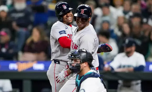 Boston Red Sox's Rafael Devers, right, celebrates his two-run home run with Enmanuel Valdez, left, next to Seattle Mariners catcher Cal Raleigh during the third inning of an opening-day baseball game Thursday, March 28, 2024, in Seattle. (AP Photo/Lindsey Wasson)