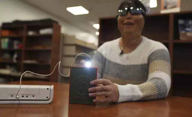 Minh Ha, assistive technology manager at the Perkins School for the Blind tries a LightSound device for the first time at the school's library in Watertown, Mass., on March 2, 2024. As eclipse watchers look to the skies in April 2024, new technology will allow people who are blind or visually impaired to hear and feel the celestial event. (AP Photo/Mary Conlon)