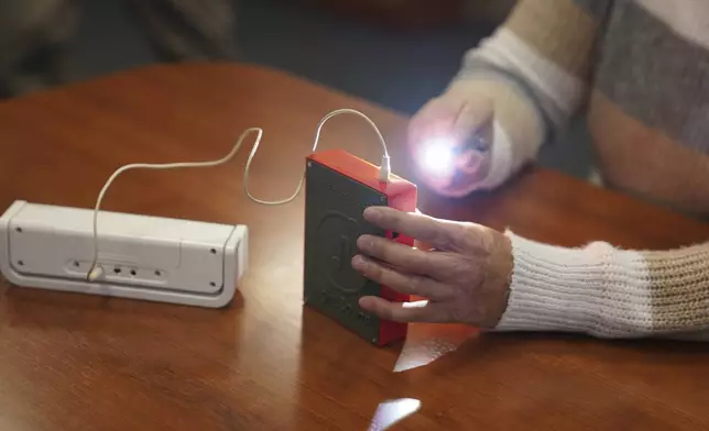 Minh Ha, assistive technology manager at the Perkins School for the Blind uses a flashlight to try a LightSound device, attached to an external speaker, for the first time at the school's library in Watertown, Mass., on March 2, 2024. Wanda Díaz-Merced, an astronomer who is blind, a co-creator of the device, says, “The sky belongs to everyone. And if this event is available to the rest of the world, it has to be available for the blind, too. ... I want students to be able to hear the eclipse, to hear the stars." (AP Photo/Mary Conlon)