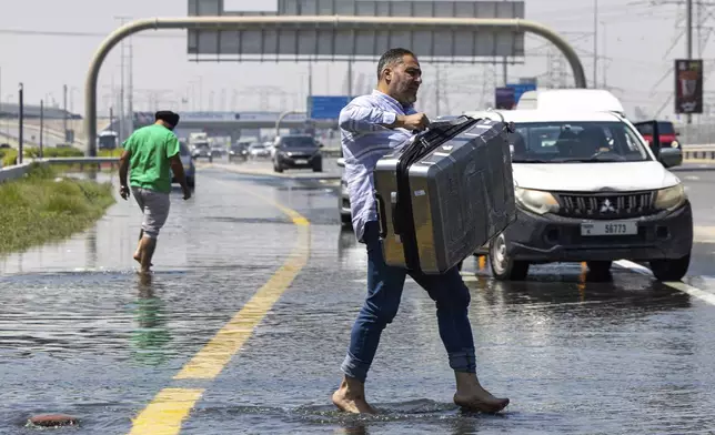 A man carries luggage through floodwater caused by heavy rain while waiting for transportation on Sheikh Zayed Road highway in Dubai, United Arab Emirates, Thursday, April 18, 2024. The United Arab Emirates attempted to dry out Thursday from the heaviest rain the desert nation has ever recorded, a deluge that flooded out Dubai International Airport and disrupted flights through the world's busiest airfield for international travel. (AP Photo/Christopher Pike)