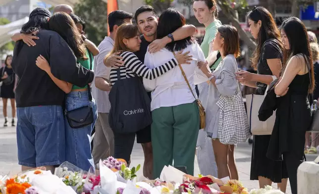 A group of people react after placing flowers as a tribute near a crime scene at Bondi Junction in Sydney, Monday, April 15, 2024, after several people were stabbed to death at a shopping on April 13. Australian police are examining why a lone assailant who stabbed several people to death in a busy Sydney shopping mall and injured more than a dozen others targeted women while avoiding men. (AP Photo/Mark Baker)
