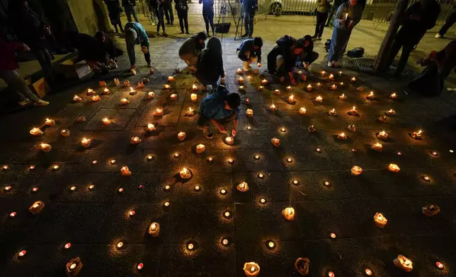 People light candles during a vigil for three police officer in front of Chile's police headquarters in Santiago, Chile, Saturday, April 27, 2024. Armed assailants ambushed and killed three law enforcement officers in southern Chile on Saturday before setting their car on fire, authorities said. (AP Photo/Esteban Felix)