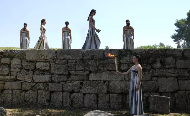 Actress Mary Mina, playing the high priestess holds a torch with the flame during the final dress rehearsal of the flame lighting ceremony for the Paris Olympics, at the Ancient Olympia site, Greece, Monday, April 15, 2024. The flame for the Paris Olympics will be officially lit Tuesday at the birthplace of the ancient games, and will then be carried through Greece for 11 days before being handed over to Paris organizers on April 26. (AP Photo/Petros Giannakouris)
