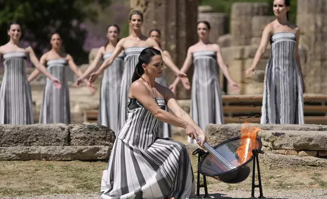 Actress Mary Mina, playing a priestess, lights the flame during the final dress rehearsal of the flame lighting ceremony for the Paris Olympics, at the Ancient Olympia site, Greece, Monday, April 15, 2024. The flame for the Paris Olympics will be officially lit Tuesday at the birthplace of the ancient games, and will then be carried through Greece for 11 days before being handed over to Paris organizers on April 26. (AP Photo/Thanassis Stavrakis)