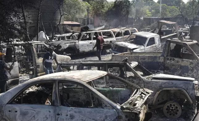 People look for salvageable pieces from burned cars at a mechanic shop that was set on fire during violence by armed gangs in Port-au-Prince, Haiti, Monday, March 25, 2024. (AP Photo/Odelyn Joseph)