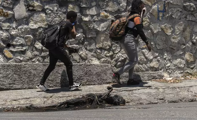 EDS NOTE: GRAPHIC CONTENT - Pedestrians walk past a charred body in Port-au-Prince's Petion-Ville neighborhood, Haiti, Sunday, April 21, 2024. (AP Photo/Ramon Espinosa)