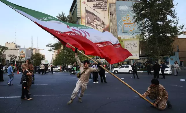 Demonstrators wave a huge Iranian flag in their anti-Israeli gathering in front of an anti-Israeli banner on the wall of a building at the Felestin (Palestine) Sq. in Tehran, Iran, Monday, April 15, 2024. World leaders are urging Israel not to retaliate after Iran launched an attack involving hundreds of drones, ballistic missiles and cruise missiles. The sign on the banner reads in Hebrew: "Your next mistake will be the end of your fake country." And the sign in Farsi reads: "The next slap will be harder." (AP Photo/Vahid Salemi)