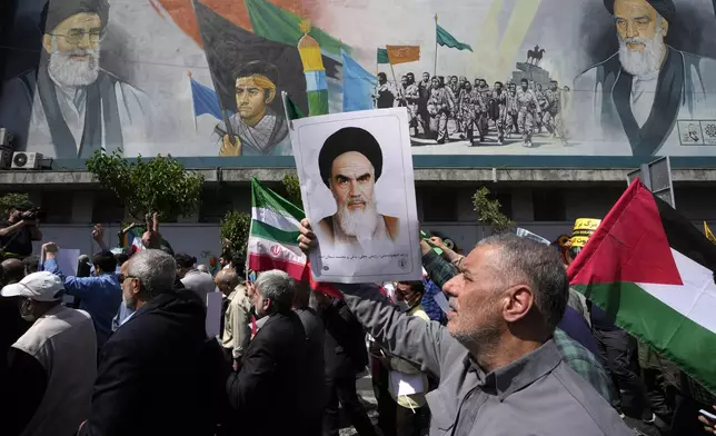 Iranian worshippers walk past a mural showing the late revolutionary founder Ayatollah Khomeini, right, Supreme Leader Ayatollah Ali Khamenei, left, and Basij paramilitary force, as they hold posters of Ayatollah Khomeini and Iranian and Palestinian flags in an anti-Israeli gathering after Friday prayers in Tehran, Iran, Friday, April 19, 2024. An apparent Israeli drone attack on Iran saw troops fire air defenses at a major air base and a nuclear site early Friday morning near the central city of Isfahan, an assault coming in retaliation for Tehran's unprecedented drone-and-missile assault on the country. (AP Photo/Vahid Salemi)
