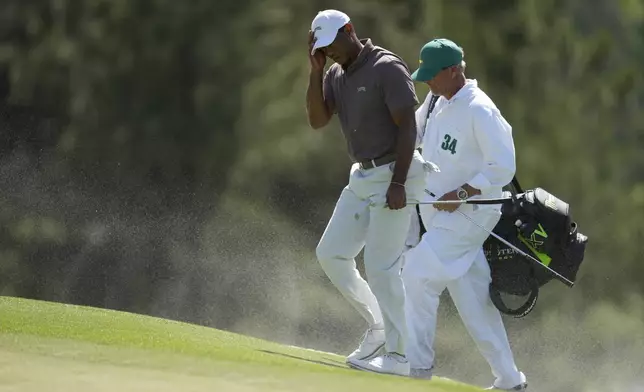 Tiger Woods and caddie Lance Bennett shield, their faces form the blowing sand on the 18th hole during second round at the Masters golf tournament at Augusta National Golf Club Friday, April 12, 2024, in Augusta, Ga. (AP Photo/Ashley Landis)